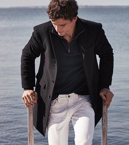 Man in white jeans, black sport coat & half-zip sweater